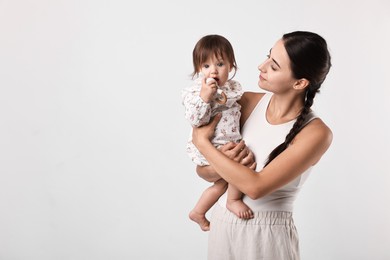 Photo of Beautiful young mother and her cute little baby with rattle on light grey background, space for text