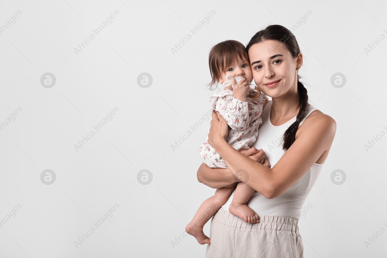 Photo of Beautiful young mother and her cute little baby with rattle on light grey background, space for text