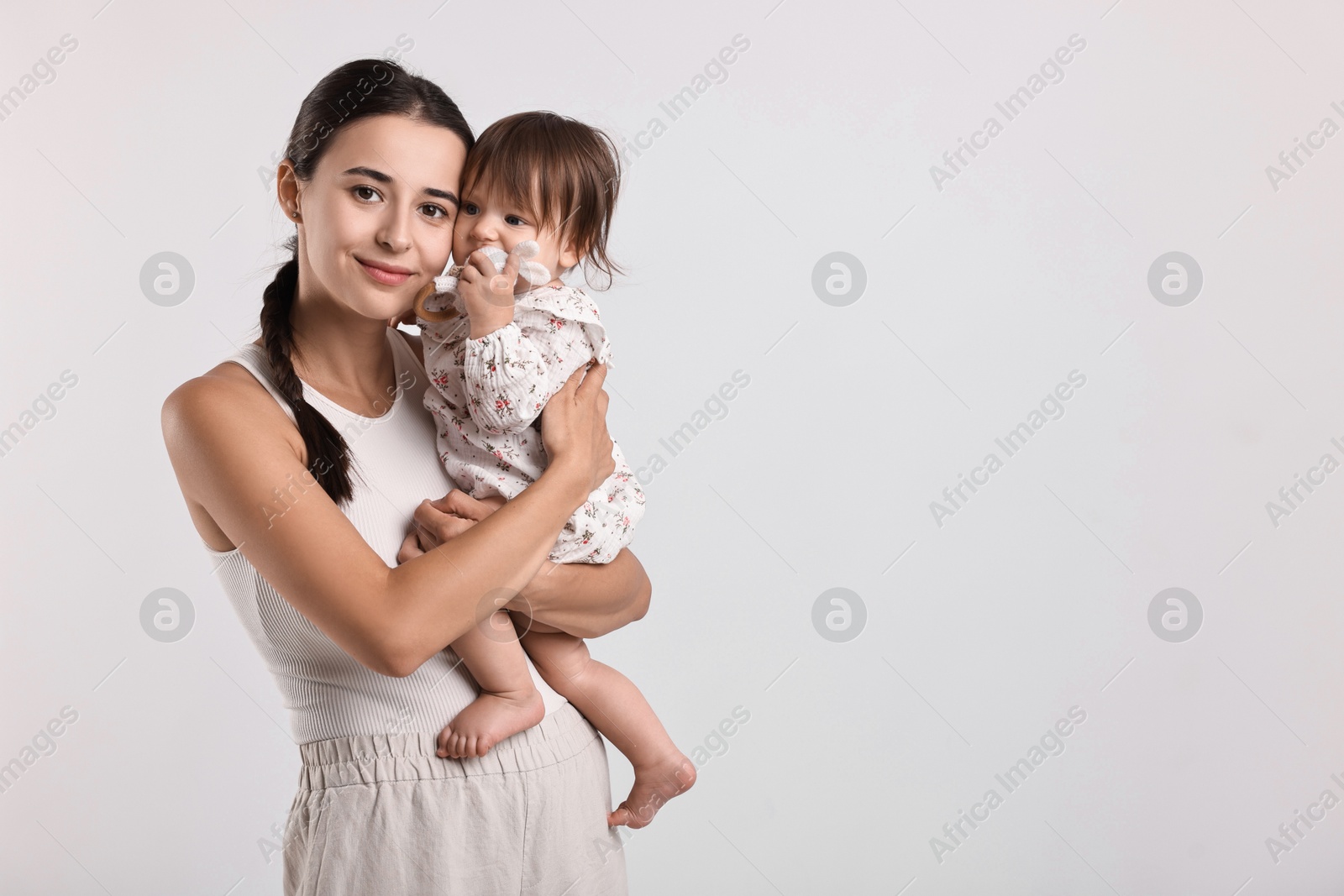 Photo of Beautiful young mother and her cute little baby with rattle on light grey background, space for text