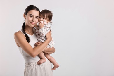 Beautiful young mother and her cute little baby with rattle on light grey background, space for text