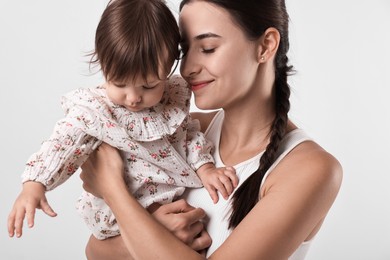 Beautiful young mother and her cute little baby on light grey background