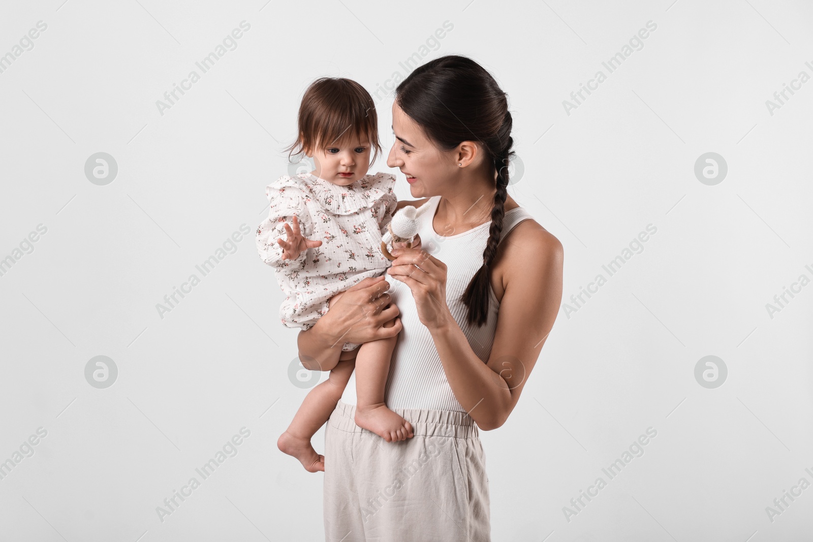 Photo of Beautiful young mother and her cute little baby with rattle on light grey background