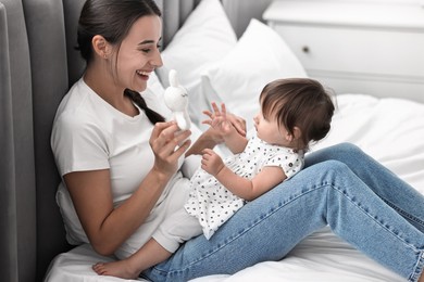 Beautiful young mother and her cute little baby with rabbit toy on bed at home