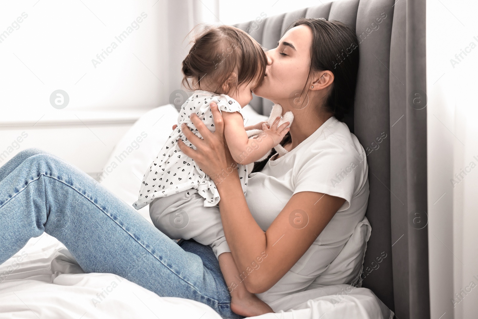 Photo of Beautiful young mother and her cute little baby with rabbit toy on bed at home