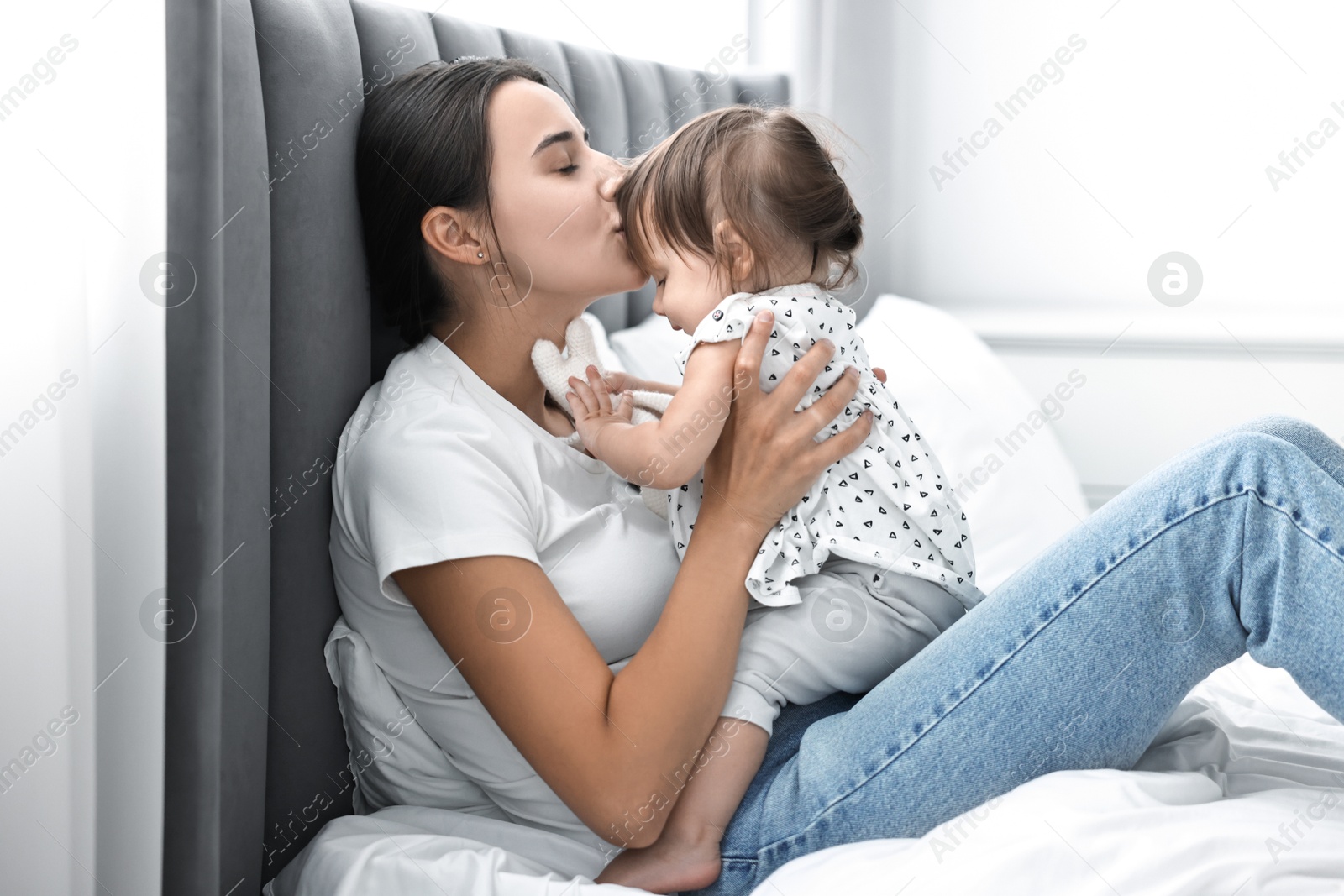 Photo of Beautiful young mother and her cute little baby with rabbit toy on bed at home