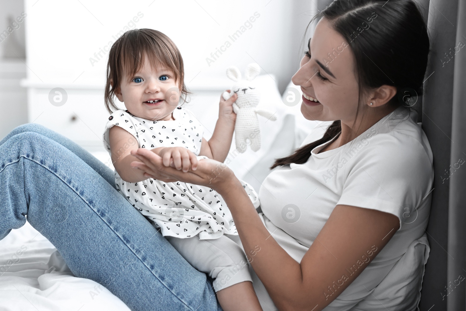 Photo of Beautiful young mother and her cute little baby with rabbit toy on bed at home