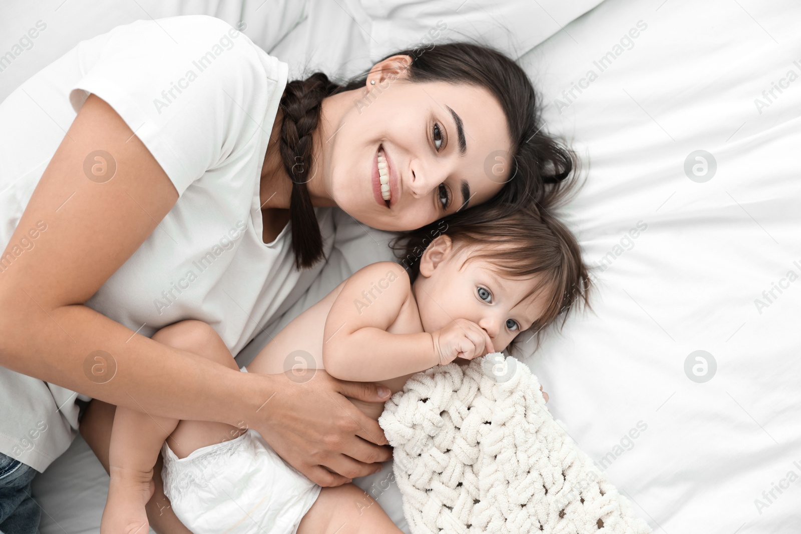 Photo of Beautiful young mother with her cute little baby on bed, top view