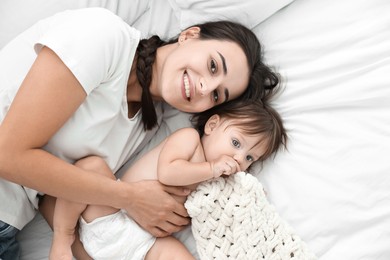 Beautiful young mother with her cute little baby on bed, top view