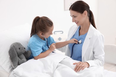 Doctor examining little girl on bed at hospital