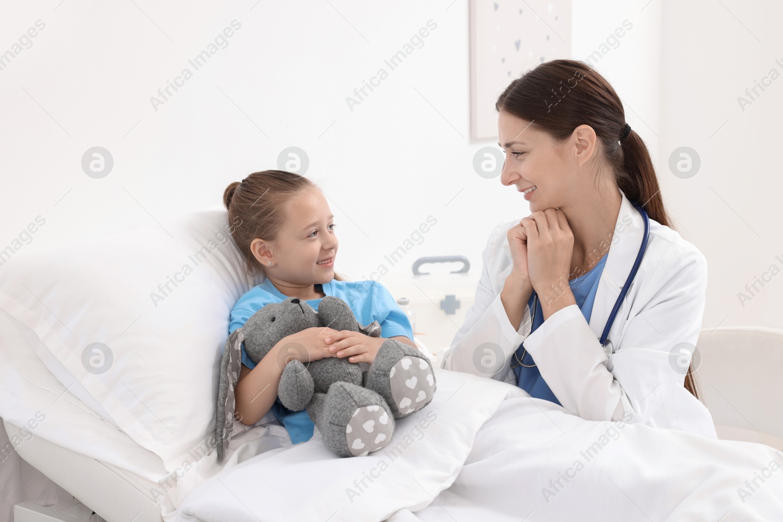 Photo of Doctor examining little girl on bed at hospital