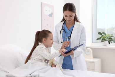 Doctor examining little girl on bed at hospital