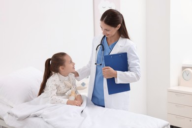 Doctor examining little girl on bed at hospital