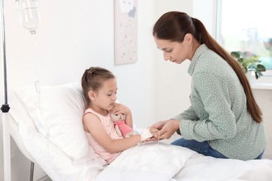 Mother and her little daughter with IV drip on bed in hospital