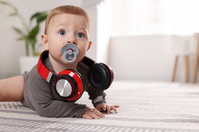 Photo of Cute little baby with pacifier and headphones on floor at home