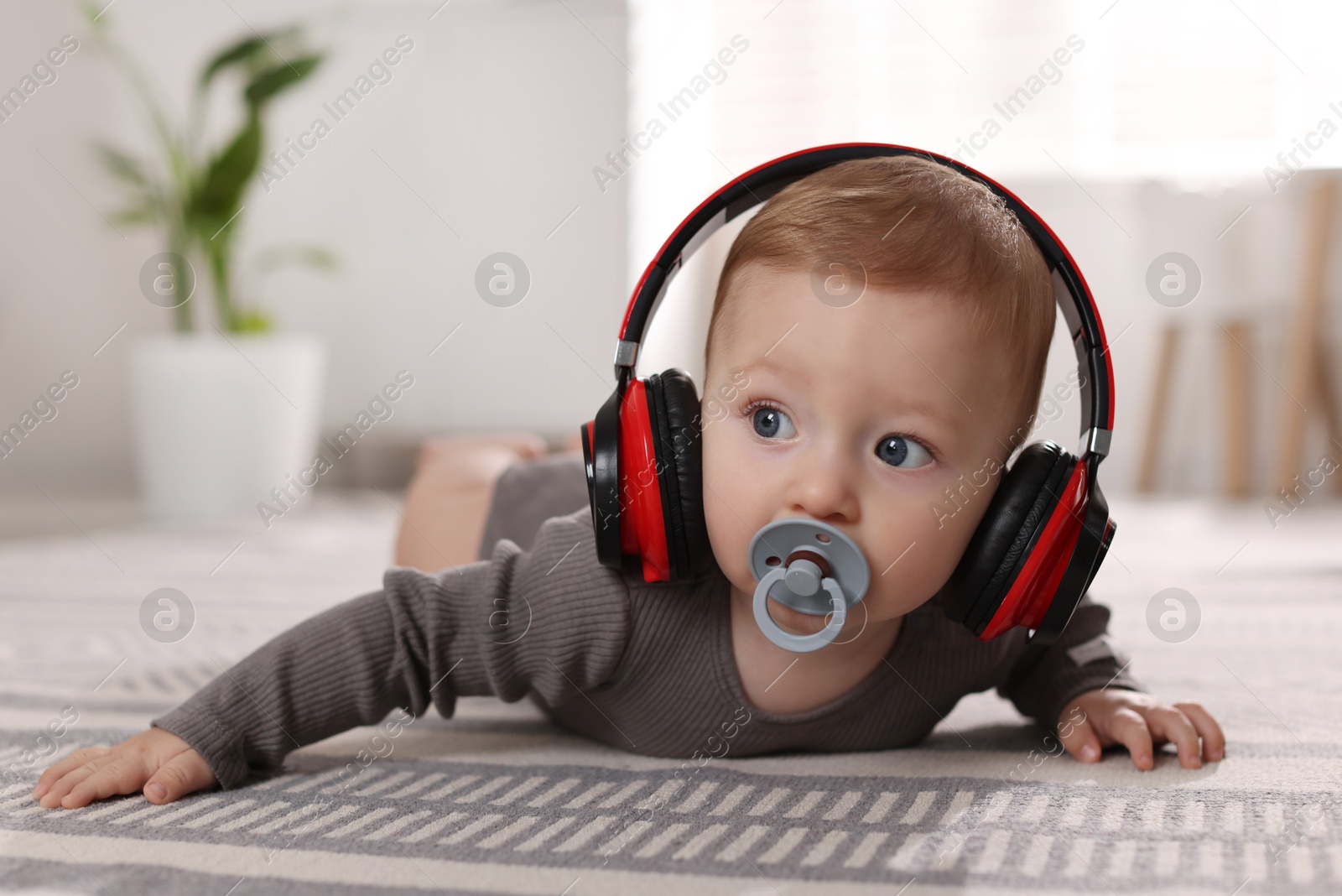 Photo of Cute little baby with pacifier and headphones on floor at home