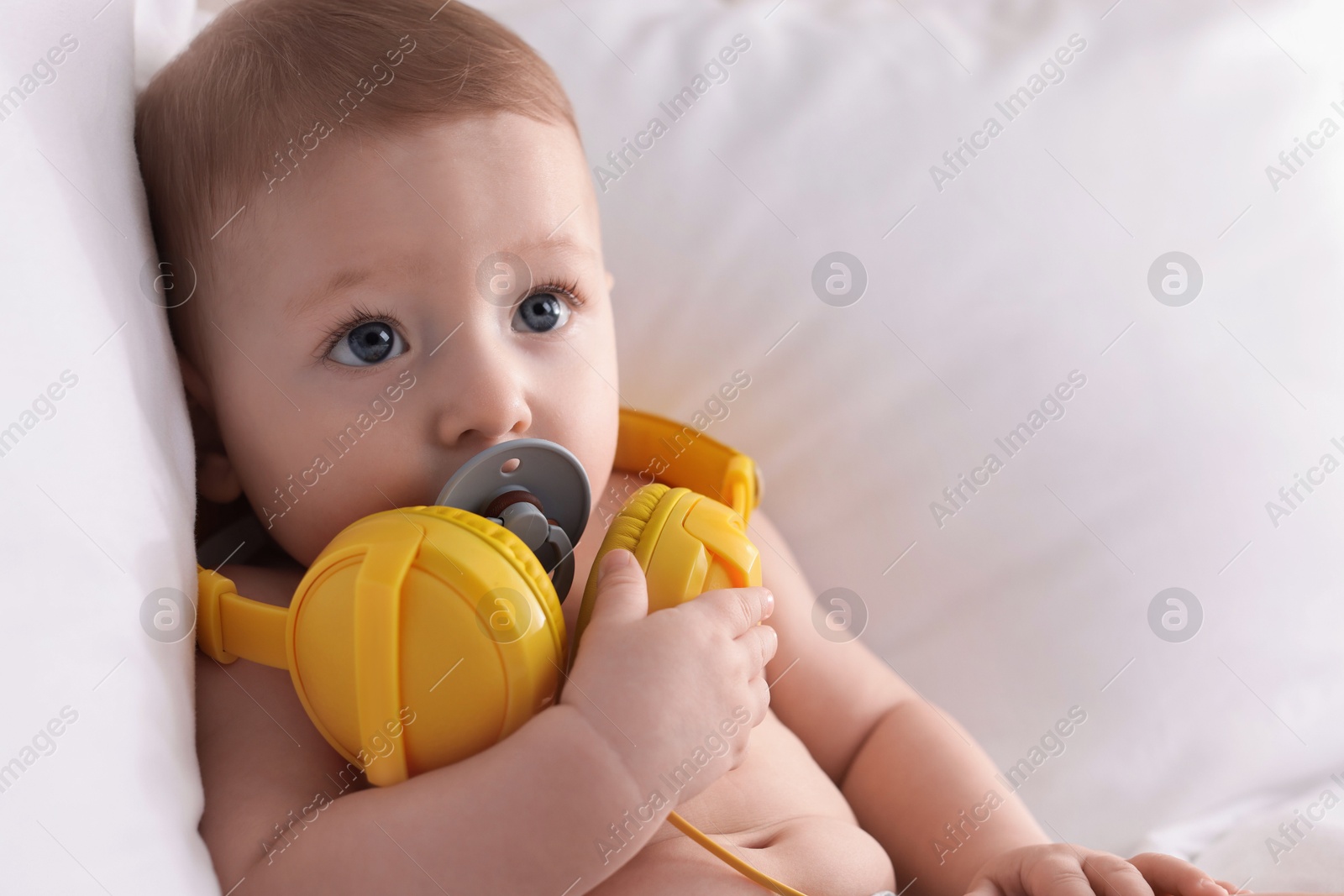 Photo of Cute little baby with headphones and pacifier on bed at home