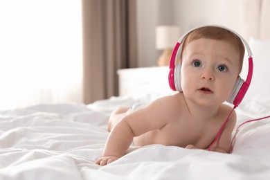 Cute little baby with headphones on bed at home, space for text