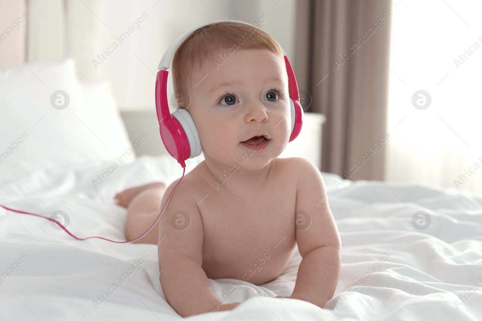 Photo of Cute little baby with headphones on bed at home