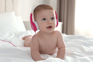 Cute little baby with headphones on bed at home