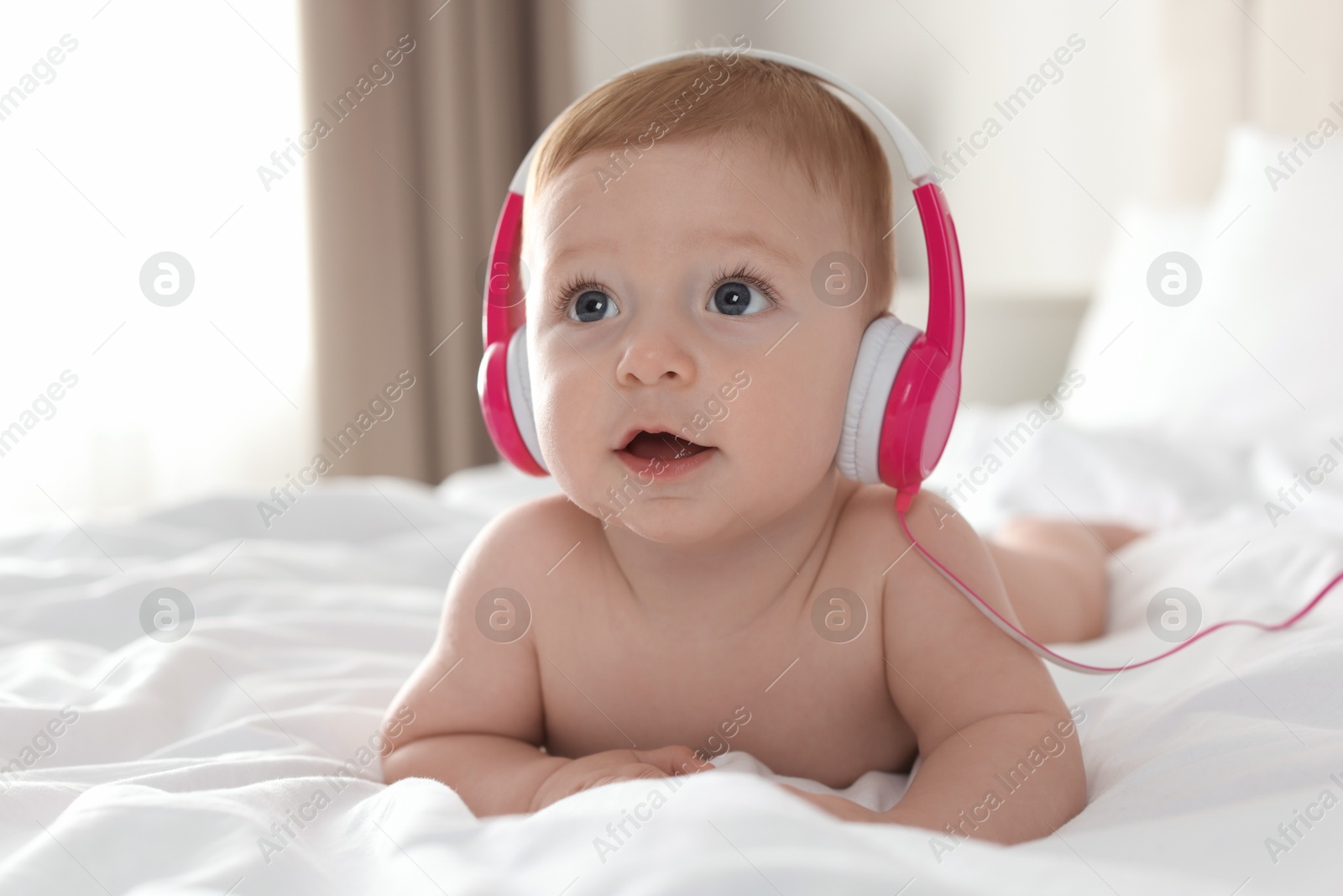 Photo of Cute little baby with headphones on bed at home