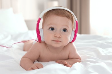 Photo of Cute little baby with headphones on bed at home