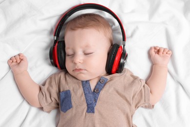 Photo of Cute little baby with headphones sleeping on bed, top view