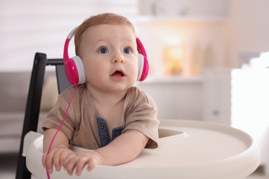 Cute little baby with headphones on high chair at home, space for text