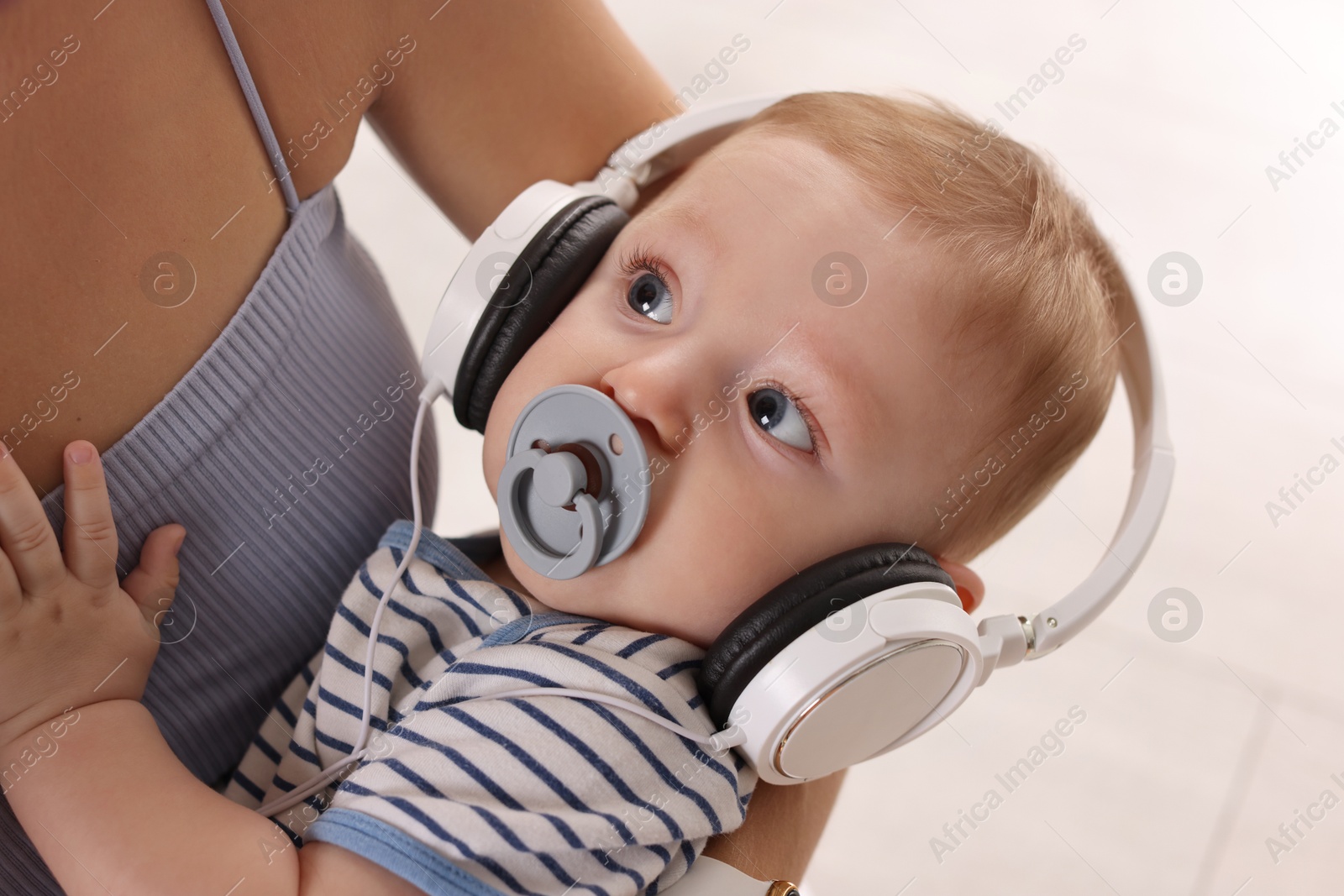 Photo of Mother holding her cute little baby with headphones and pacifier at home, closeup