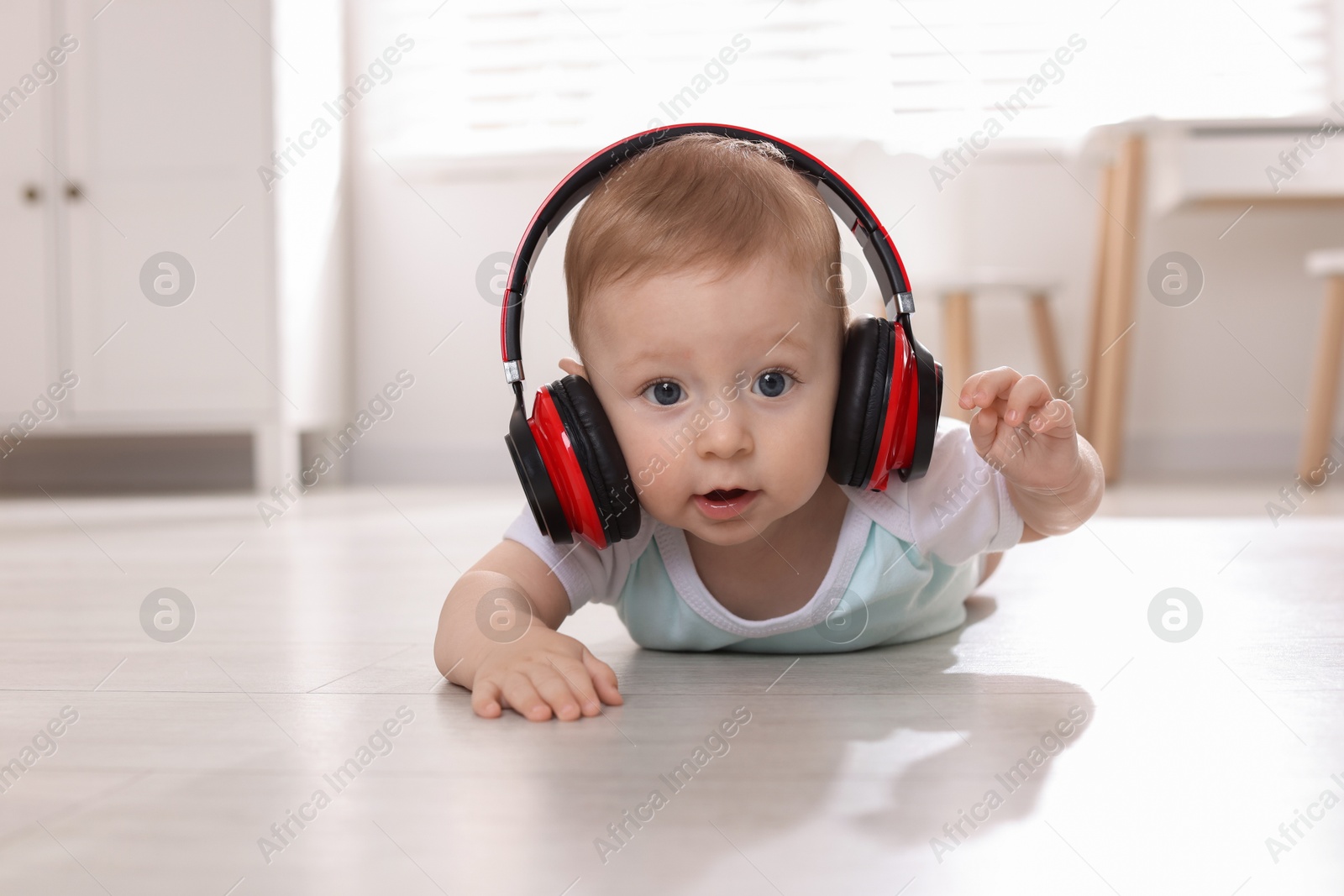 Photo of Cute little baby with headphones on floor at home