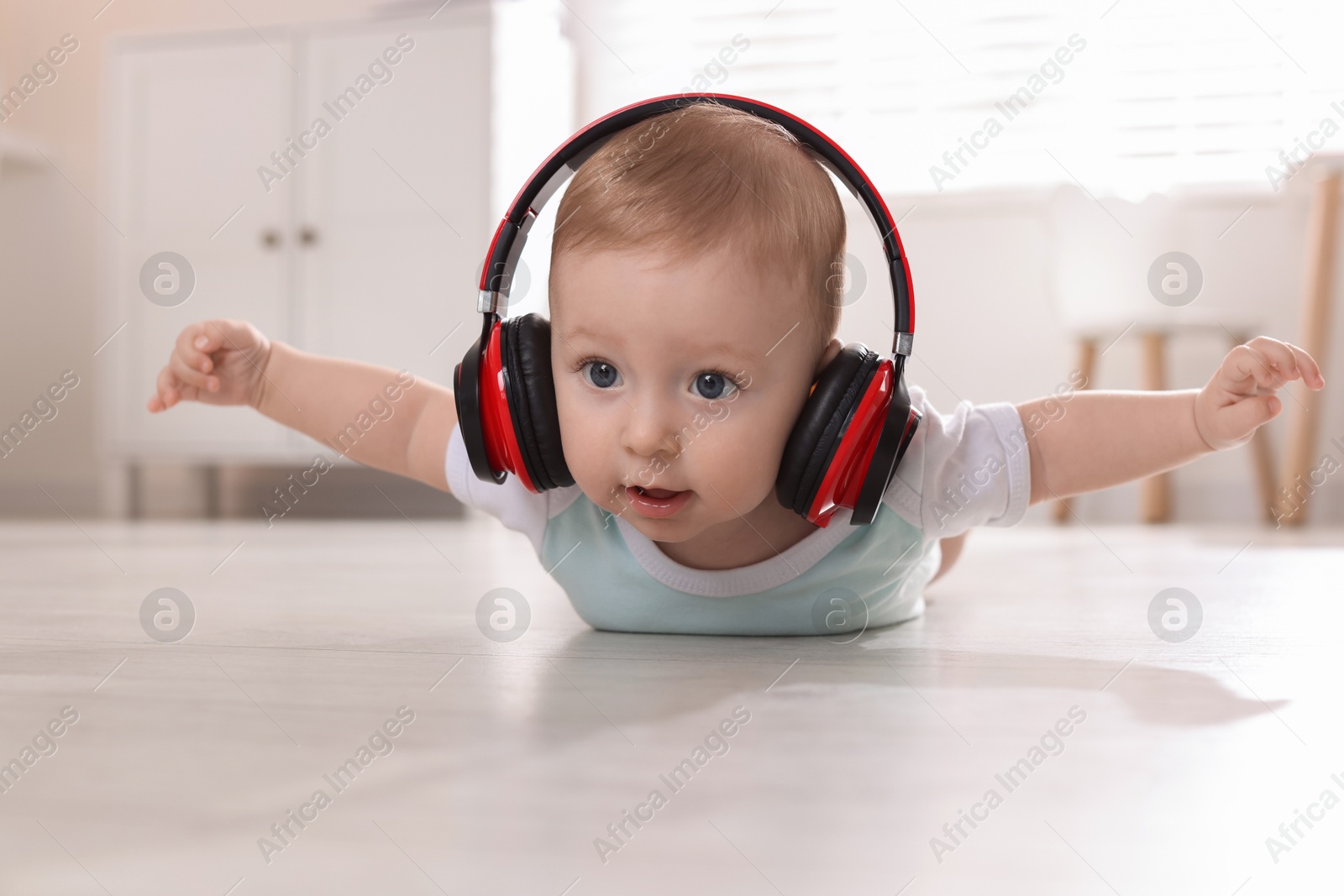 Photo of Cute little baby with headphones on floor at home