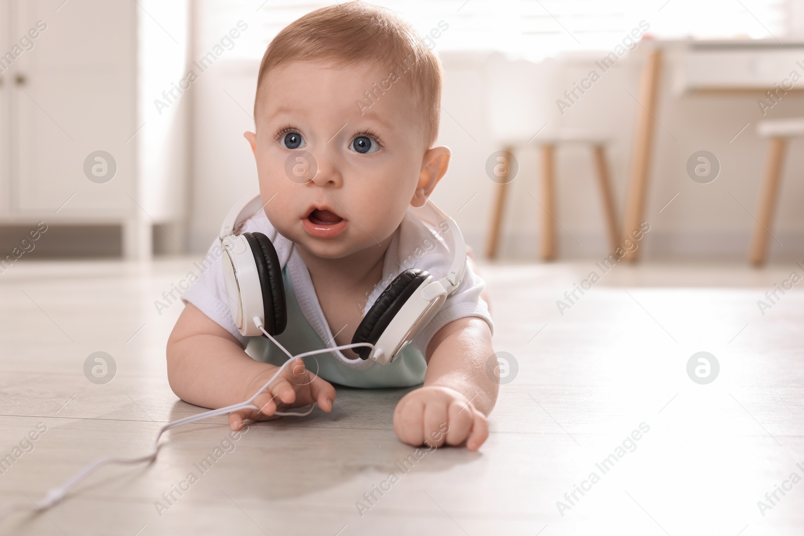 Photo of Cute little baby with headphones on floor at home, space for text