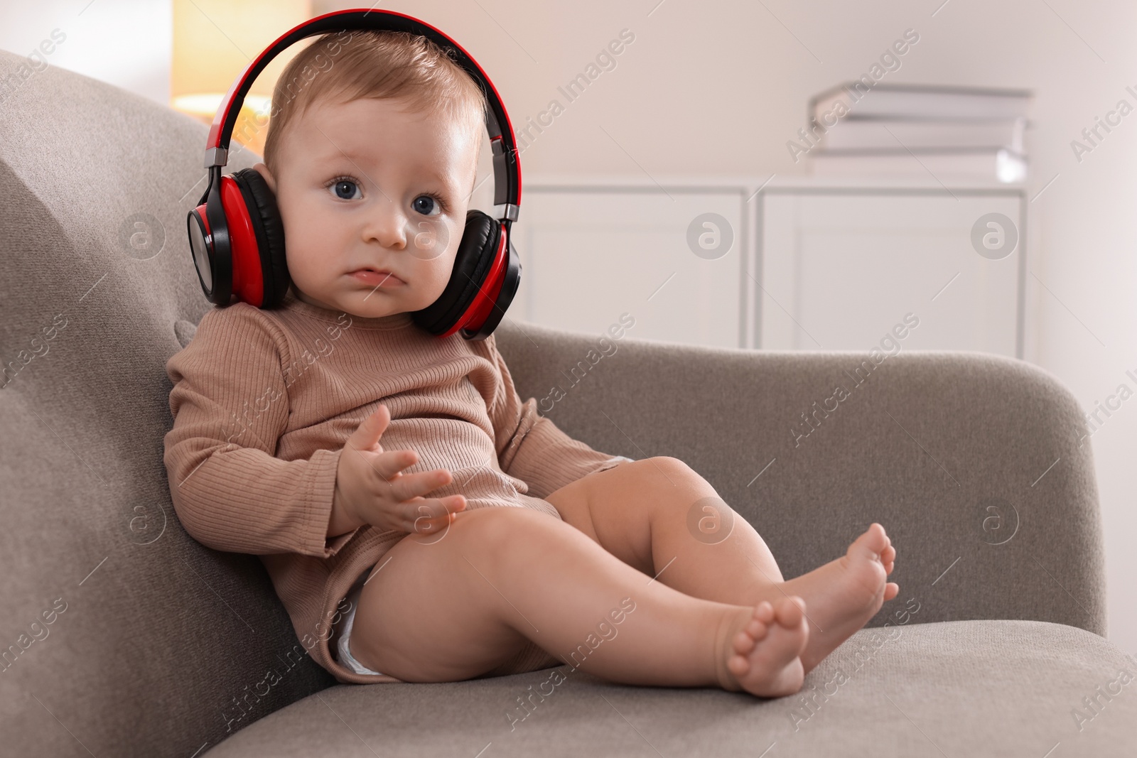 Photo of Cute little baby with headphones on sofa at home, space for text