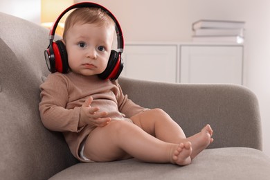 Cute little baby with headphones on sofa at home, space for text