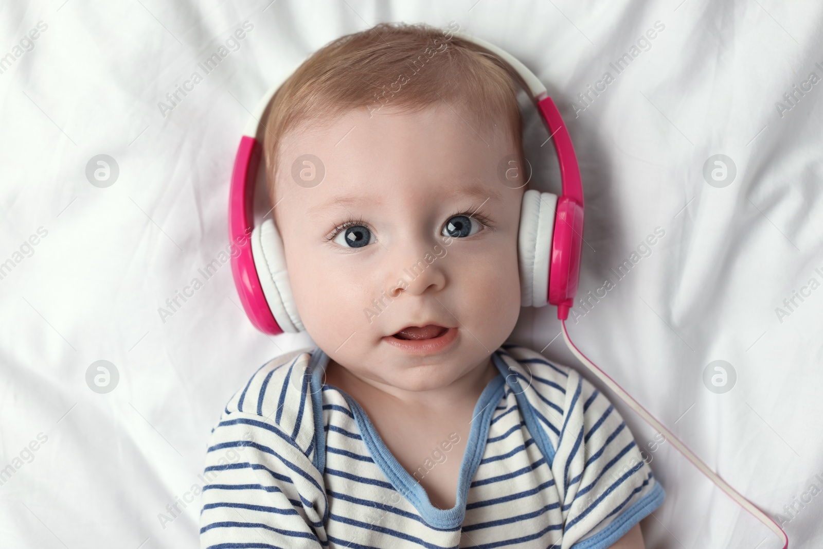 Photo of Cute little baby with headphones lying on bed, top view