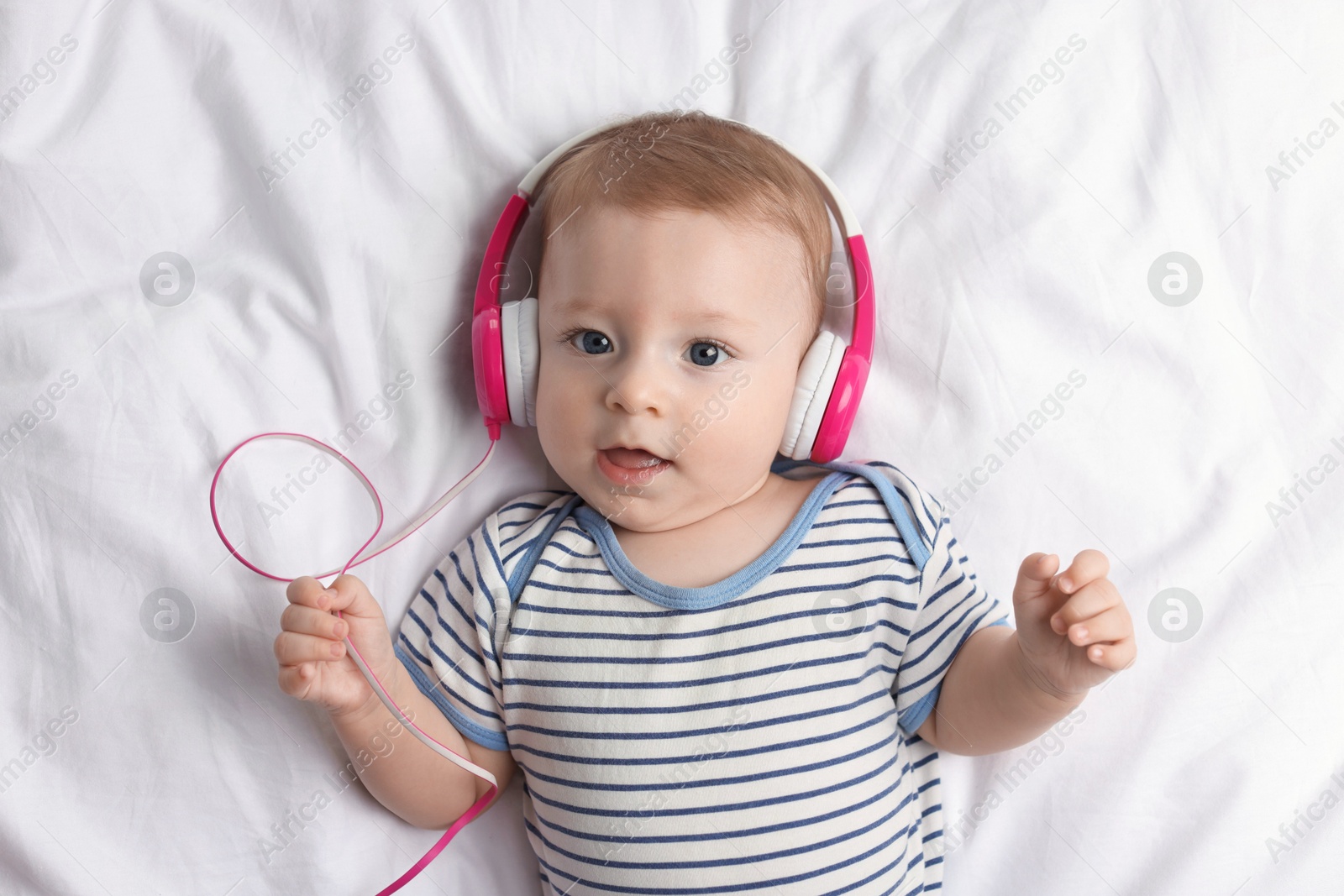 Photo of Cute little baby with headphones lying on bed, top view