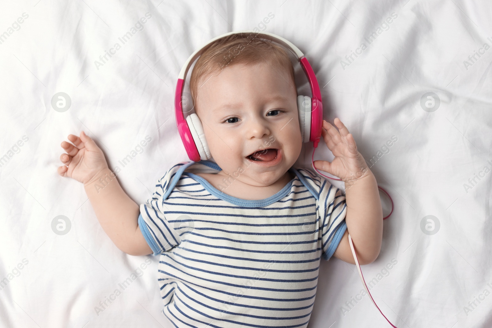 Photo of Cute little baby with headphones lying on bed, top view