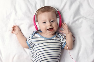 Cute little baby with headphones lying on bed, top view