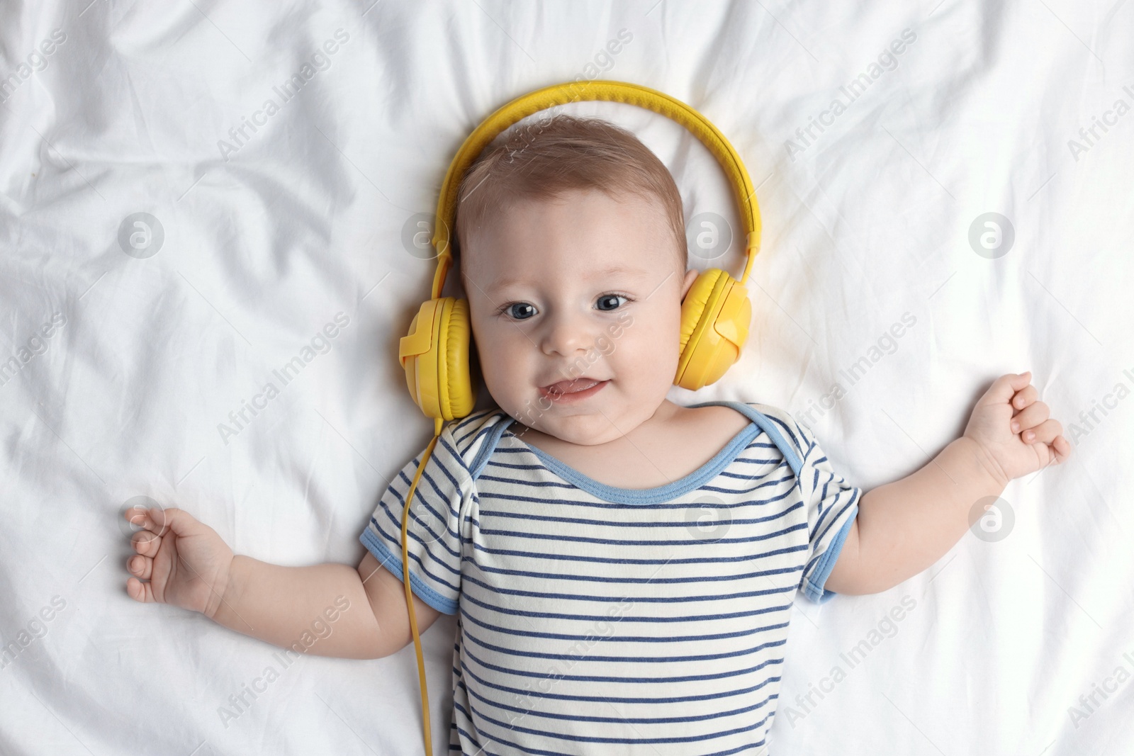 Photo of Cute little baby with headphones lying on bed, top view