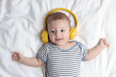 Cute little baby with headphones lying on bed, top view