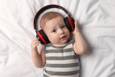 Photo of Cute little baby with headphones lying on bed, top view