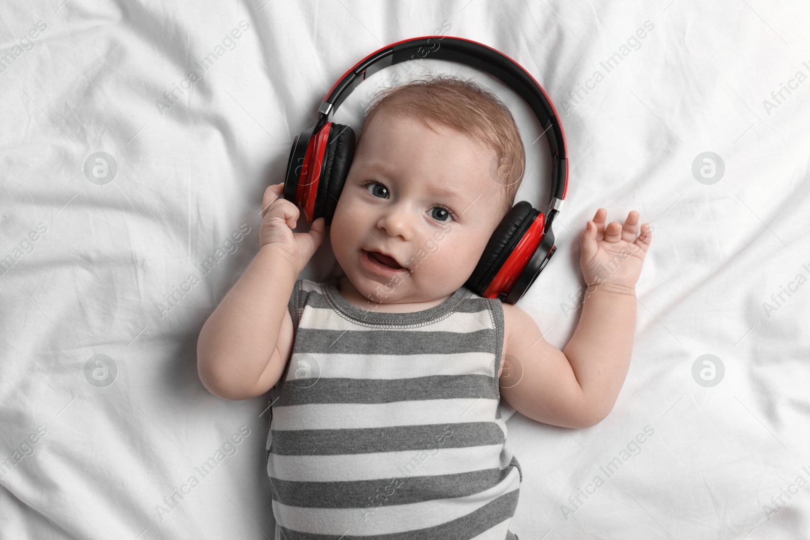 Photo of Cute little baby with headphones lying on bed, top view