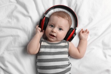 Cute little baby with headphones lying on bed, top view