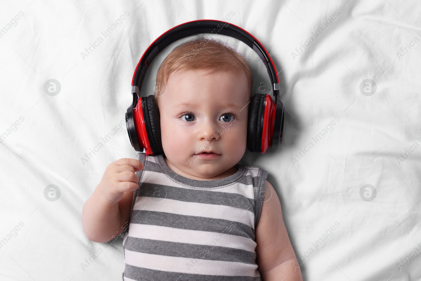 Photo of Cute little baby with headphones lying on bed, top view