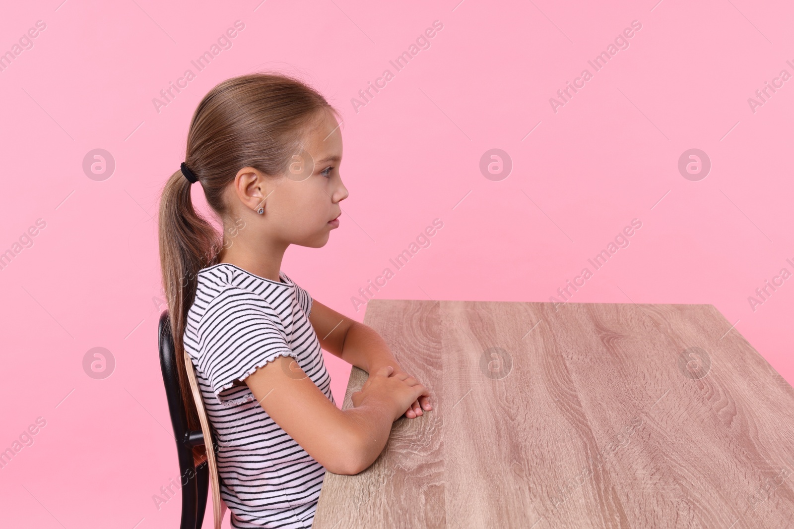 Photo of Girl with correct posture sitting at wooden desk on pink background