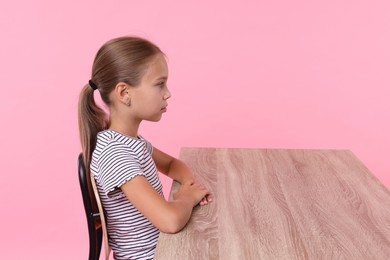 Girl with correct posture sitting at wooden desk on pink background