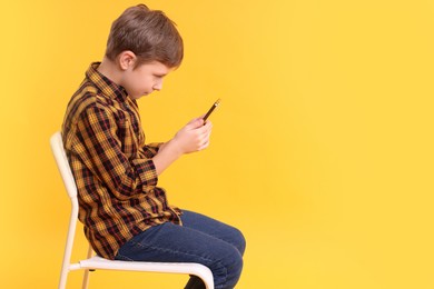 Photo of Boy with incorrect posture and smartphone sitting on chair against yellow background