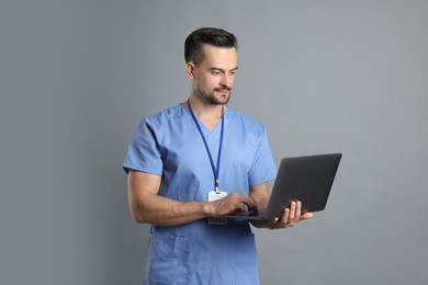 Nurse with badge using laptop on grey background