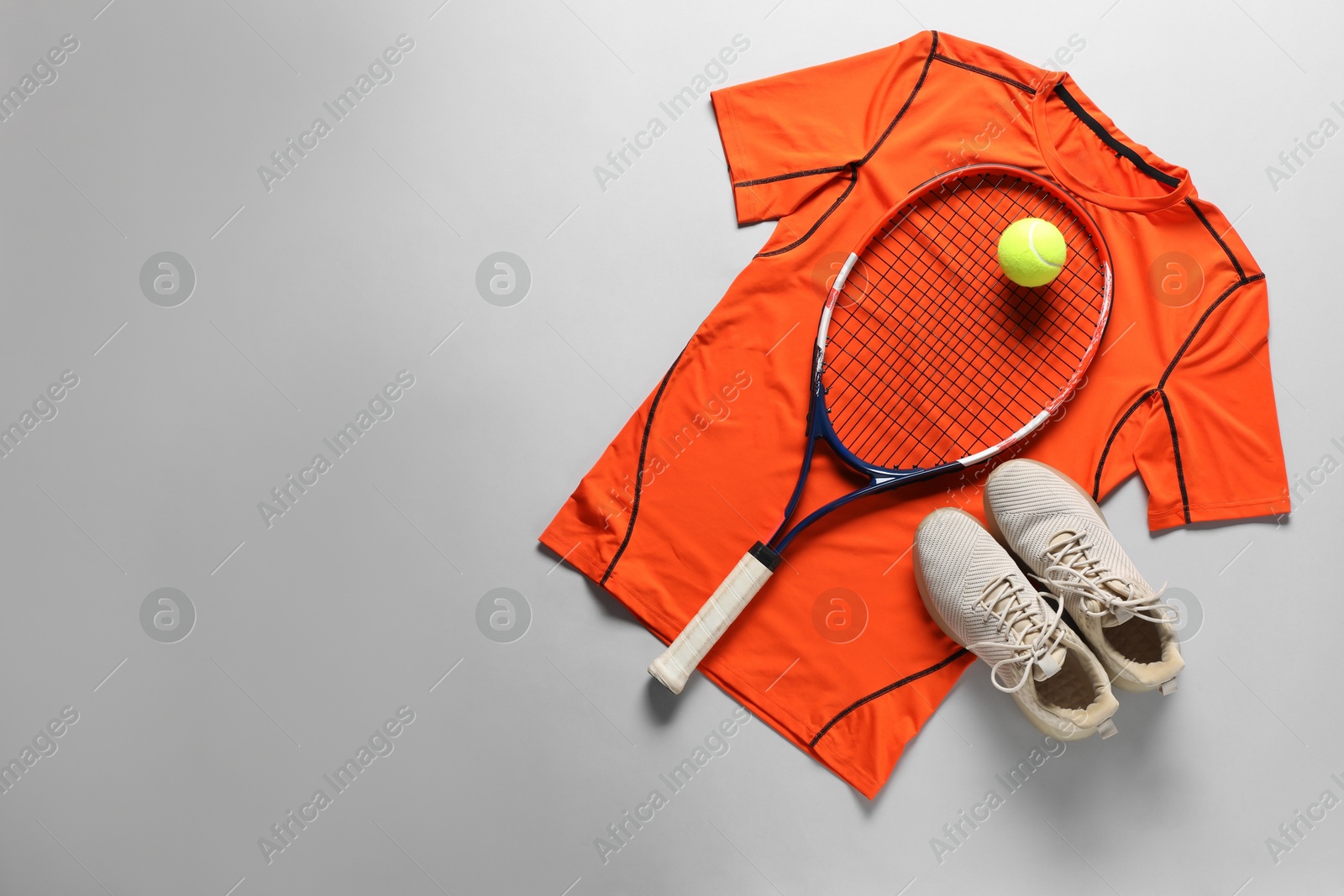 Photo of Tennis racket, ball, sneakers and orange shirt on grey background, flat lay. Space for text