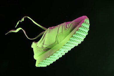 Photo of Stylish sneaker in air against dark background in neon lights