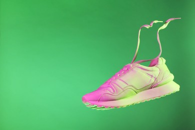 Photo of Stylish sneaker in air against green background in neon lights, space for text